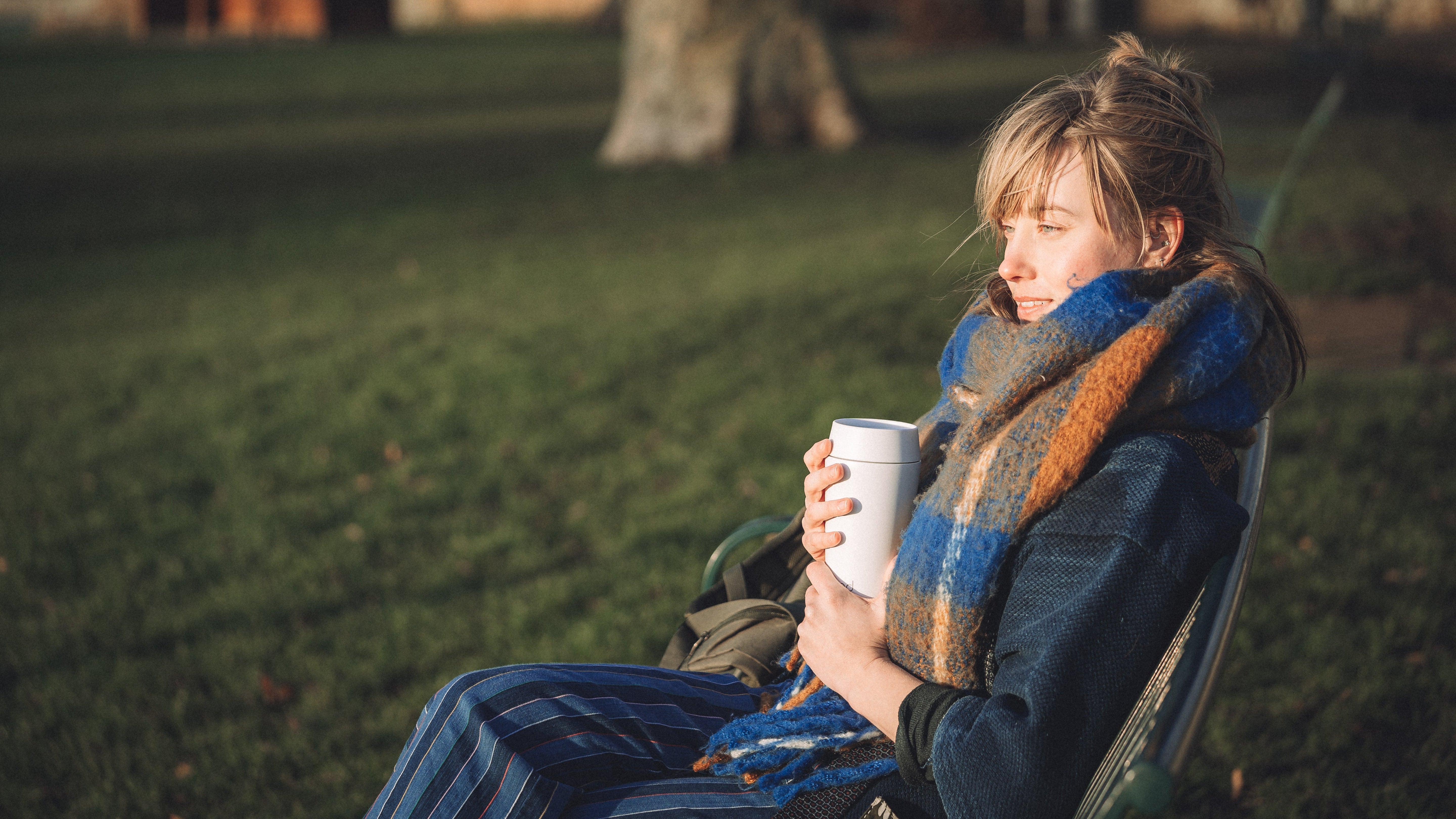 bru white insulated travel mug held by a person sitting outdoors in a park on a cold day